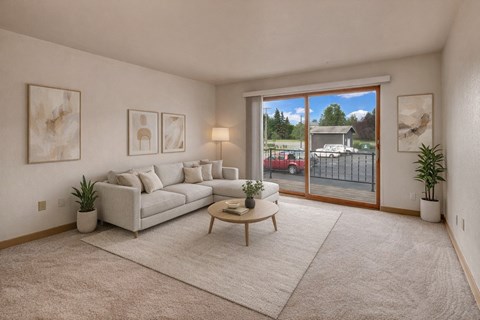 A living room with a white couch, a wooden coffee table, and a large window with a view of the outside.