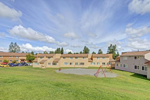 A row of houses with a green lawn and park in front.