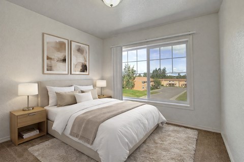 Bright bedroom here at The Glen featuring a neatly made bed with white bedding and neutral throw blanket, matching nightstands with lamps, soft carpet flooring, and a large window that brings in natural light and views of the community grounds.