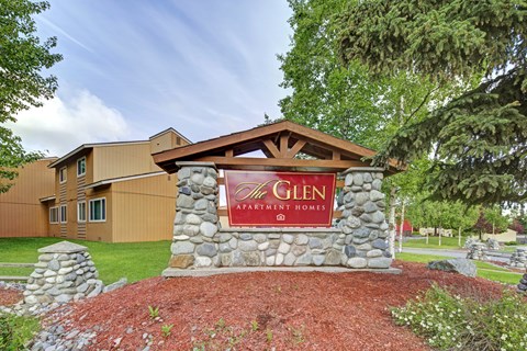 The entrance to a Glen Apartment Homes complex is framed by a stone pillar and a wooden arch.