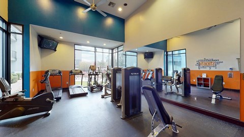 A spacious modern fitness center here at Acclaim featuring cardio machines, strength equipment, mirrored walls, high ceilings, ceiling fans, and large windows that fill the room with natural light for an energizing workout environment.