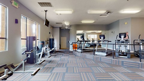 A bright community fitness center here at Arezzo featuring treadmills, ellipticals, strength training machines, mirrored walls, large windows for natural light, patterned flooring, and open workout space designed for residents to exercise comfortably and enjoy a well-equipped indoor gym.