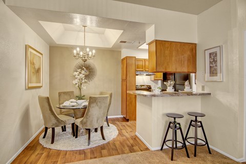 A dining room with a table set for two and a kitchen area in the background.