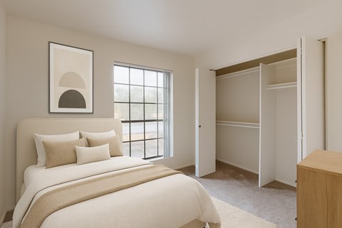 A serene bedroom here at Aspire Pinnacle Park featuring soft neutral walls, plush carpeting, and a large window that fills the space with natural light. The room includes a spacious walk-in closet with double doors and ample hanging storage, creating a bright and functional retreat with a calm, inviting atmosphere.
