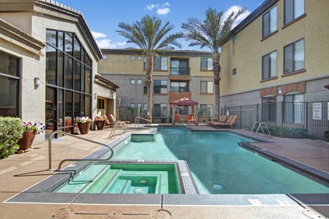 A vibrant and refreshing pool area here at Bolero featuring a sparkling swimming pool with a built-in spa and sleek tile detailing. Lounge chairs and shaded cabanas create inviting spaces to relax, while tall palm trees and surrounding architecture provide a private, resort-style atmosphere perfect for enjoying sunny days outdoors.
