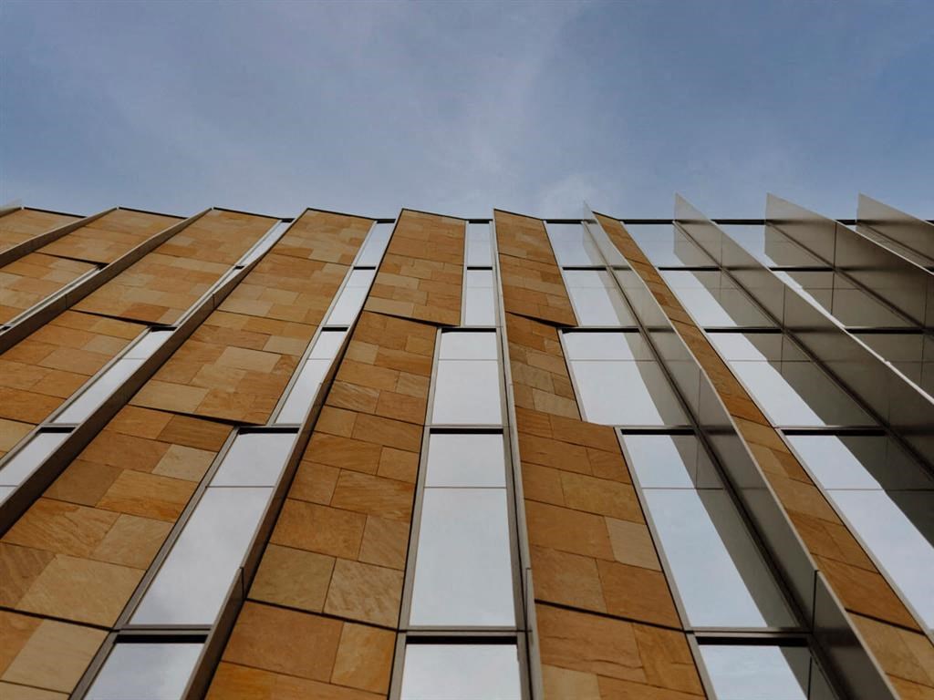 Joy on 4th's modern building facade with vertical stone panels and reflective glass, creating a dynamic geometric pattern against a clear blue sky.