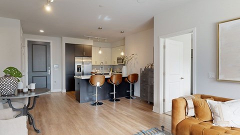A modern living room with a brown leather couch and a kitchen area in the background.
