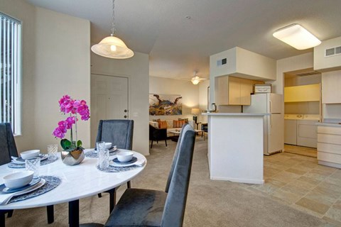 A dining room with a table set for two and a kitchen in the background.