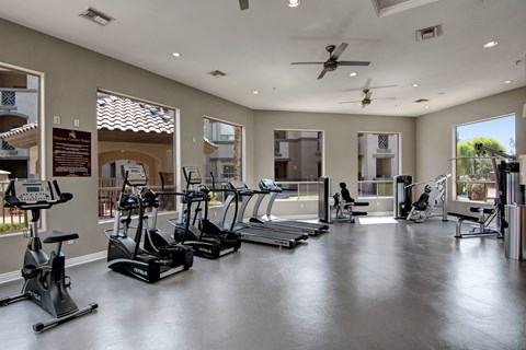 A spacious fitness center here at Sonoma Landing featuring rows of treadmills and elliptical machines, a stationary bike, and strength training equipment arranged on sleek flooring, with large windows bringing in natural light, neutral walls, ceiling fans, recessed lighting, and views of the surrounding apartment community.