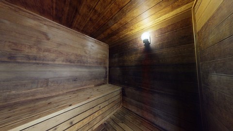 Wood-paneled sauna interior here at The Club at Eagle Pointe Apartments with soft amber lighting, highlighting a warm, rustic bench along the left wall. Cozy, inviting atmosphere.