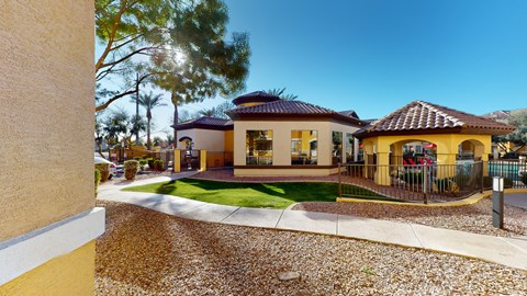 A house with a yellow and white exterior is surrounded by a gravel driveway and a metal fence.