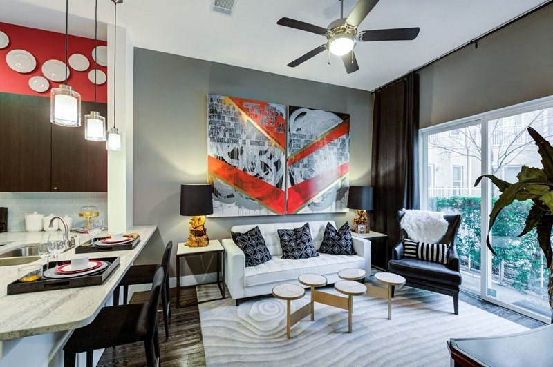 Modern living room here at Arpeggio Apartment Homes featuring a white sofa with black geometric pillows, abstract wall art, circular wooden tables, and large windows. Bright and stylish ambiance.