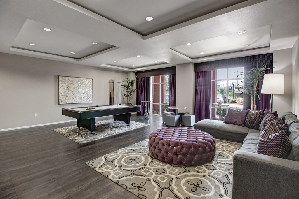 Stylish resident lounge here at Artisan at Main Street Metro Apartments with a pool table on patterned rugs, deep purple curtains, and cozy sofa with matching cushions, creating a luxurious, relaxed ambiance.