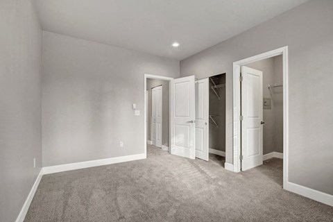 A room with carpeted floor and white walls with three open doors.