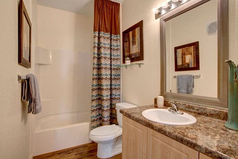 Modern bathroom here at Aspire at Pinnacle Peak Apartments with a white bathtub and a patterned curtain. A marble countertop has a sink, framed mirror, and decor. Neutral tones create a cozy feel.