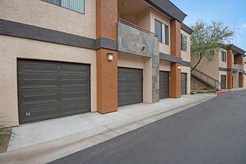 Aspire at Pinnacle Peak's modern apartment complex with beige and brown tones, featuring dark garage doors and stone accents. A tree and staircase add contrast. Calm atmosphere.