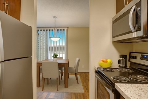 A kitchen with a refrigerator, microwave, oven, and a dining table with chairs.