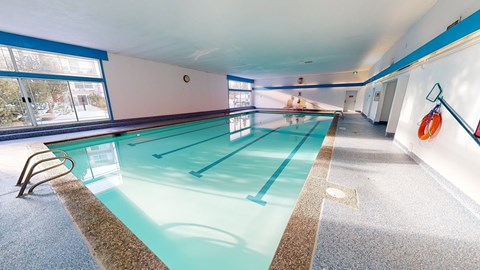 A bright indoor swimming pool here at Cambridge West with clear water, lap lanes, and wide deck space, featuring large windows for natural light and a clean, relaxing atmosphere.