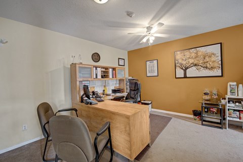 A welcoming leasing office here at Carrington Place with a spacious wooden front desk and comfortable guest seating, featuring warm accent walls, bright ceiling fan lighting, and a convenient refreshment station for a friendly, professional visit.