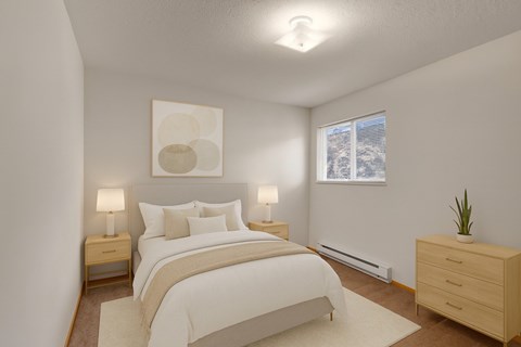 A cozy bedroom here at Carrington Place with soft carpet and neutral walls, featuring a neatly staged bed with light bedding, matching nightstands with lamps, and a large window with blinds for natural light.