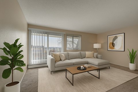A bright living room here at Cedar Gardens featuring a spacious light gray sectional with neutral throw pillows, a warm wood coffee table, and a soft area rug, complemented by large windows, simple wall art, and lush greenery for a cozy, welcoming feel.