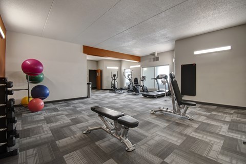 A modern fitness center here at Centre Pointe Plaza featuring a variety of cardio machines, free weights, and workout benches, with bright lighting, sleek flooring, and colorful exercise balls for an energetic, convenient space.