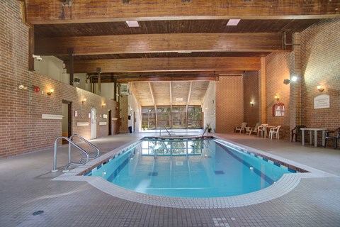 Here at Edgemont Heights, enjoy a bright indoor pool area with sparkling blue water, classic brick walls, and warm wood-beam ceilings, plus plenty of deck space with seating for relaxing.