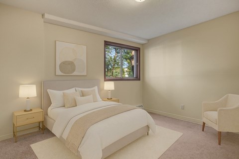 A bedroom with a large bed, a nightstand with a lamp, a chair, and a framed picture on the wall.