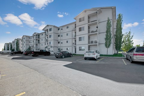 A bright exterior view here at Edgewood Estates featuring a well-maintained apartment community with private balconies, a convenient parking area, and mature trees, all set against a clear blue sky for a welcoming first impression.