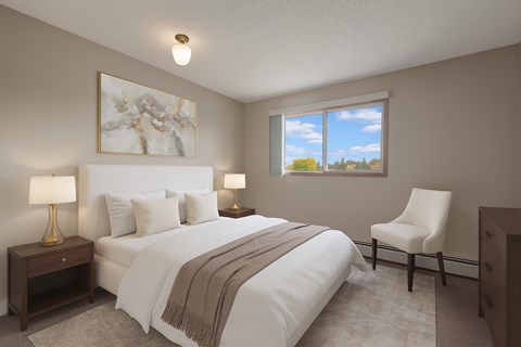 A bright bedroom here at Gateway Square featuring a cozy bed with crisp white bedding and soft neutral pillows, paired with matching nightstands and warm table lamps, plus elegant wall art and a plush accent chair for a calm, relaxing retreat.