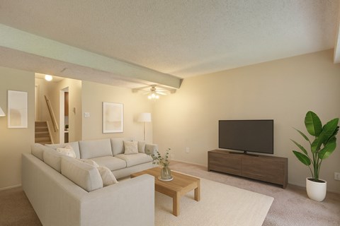 A bright, modern living room here at Lakewood Heights with a light gray sectional sofa, a wooden coffee table, neutral wall art, soft carpeted flooring, and a media console with a TV, creating a warm and inviting atmosphere.