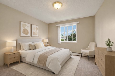 A calm, inviting bedroom here at Madison Park with beige carpet, soft neutral walls, and a large window bringing in natural light and leafy outdoor views. A neatly made bed with white bedding and layered neutral pillows sits between matching nightstands with lamps, complemented by abstract wall art, a cozy accent chair, and a light wood dresser.