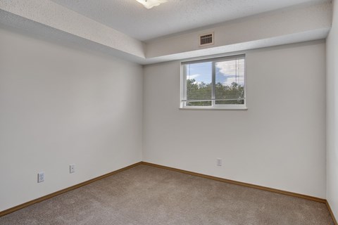 A bright, empty bedroom here at Quail Ridge with soft carpet, clean white walls, and a wide window with blinds letting in natural light. A recessed ceiling detail adds a cozy touch while keeping the space open and versatile.