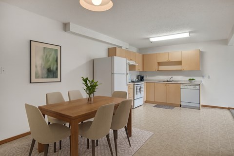 A dining room with a table and chairs and a kitchen in the background.