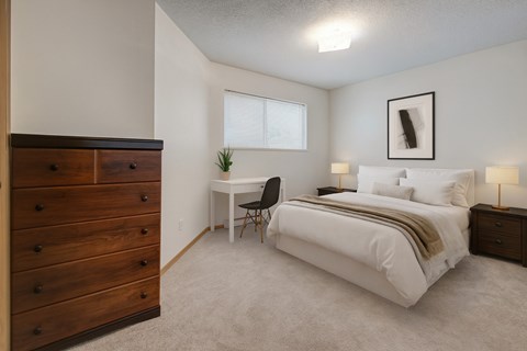 A bedroom with a bed, desk, chair, and dresser.