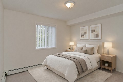 A serene bedroom here at Somerset Pointe featuring a plush neutral bed with layered white bedding and soft accent pillows, matching nightstands with warm table lamps, light carpeting, minimalist wall art above the headboard, and a window with vertical blinds that brings in gentle natural light.