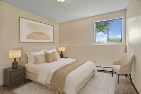 A serene bedroom here at Ventana featuring a queen-sized bed with crisp white bedding, layered neutral pillows, and a soft beige throw, complemented by matching bedside tables with lamps, abstract wall art above the headboard, plush carpeting, a cozy accent chair, and a bright window bringing in natural light.