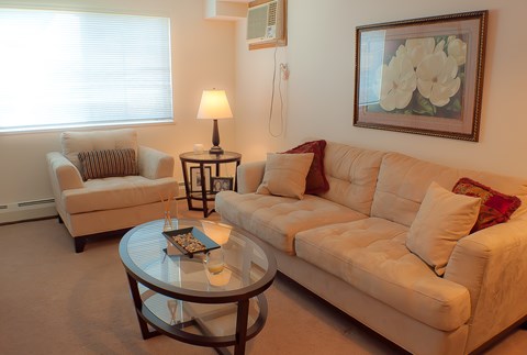 A living room with a white couch, a glass table, and a painting on the wall.
