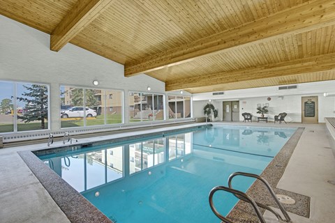 A bright indoor swimming pool here at Wyndham Crossing with clear blue water, a wide deck area, and stainless steel handrails for easy access. Large windows line the wall to bring in natural light, and the warm wood-beam ceiling adds a welcoming touch to the space.