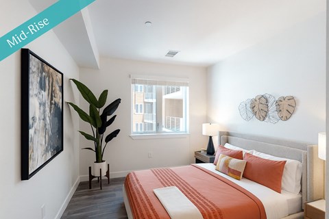 A bedroom with a bed, a plant, and a painting on the wall.