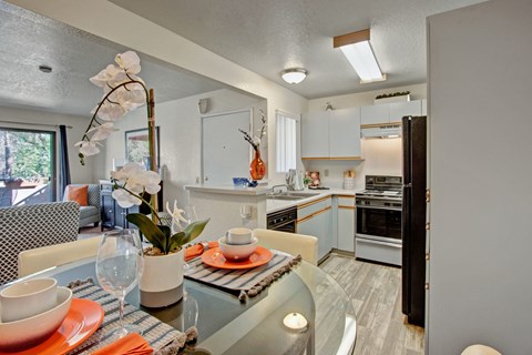A modern kitchen with a glass table and orange accents.