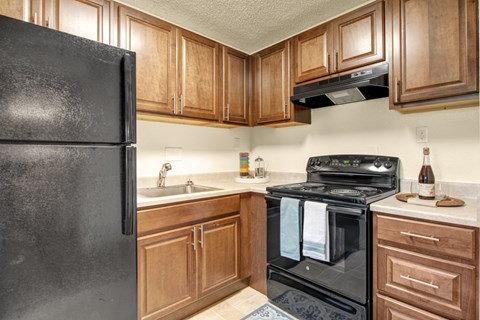 A black refrigerator is in a kitchen with wooden cabinets.
