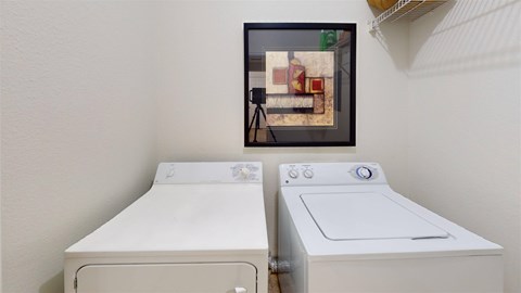An in-home laundry area here at Camelback Pointe featuring a full-size washer and dryer side by side, neutral walls, and framed artwork above for a clean, finished look.