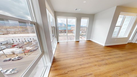 A bright open living and dining area here at Experience at Epicenter featuring wide wood-style flooring, an accent wall, and expansive windows with simple shades that overlook the surrounding neighborhood. A modern pendant light defines the dining space, while the open layout and natural light create a spacious, airy setting ideal for relaxing or entertaining.