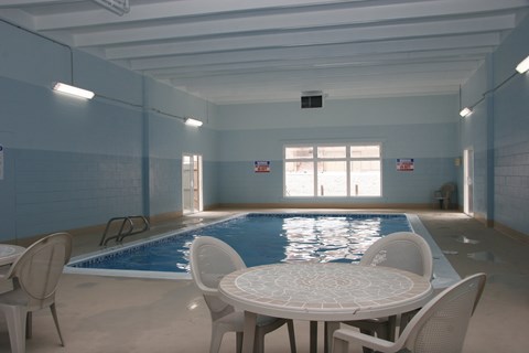 A spacious indoor pool area here at Hyde Park North Apartments with a rectangular swimming pool surrounded by a concrete deck. Natural light enters through large windows, while poolside tables and chairs offer space to relax. Light blue walls, overhead lighting, and easy pool access create a comfortable, year-round amenity.