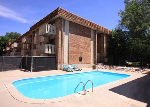 A refreshing outdoor pool area here at Hyde Park Apartments with a clear rectangular swimming pool surrounded by a concrete deck. Lounge chairs sit nearby for relaxing, while a brick apartment building with balconies and surrounding trees creates a private, inviting community atmosphere.