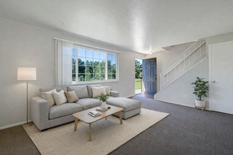 A living room with a grey couch, a wooden coffee table, and a staircase.