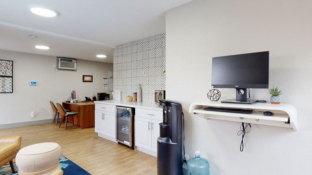Modern leasing office here at Hillside Village Apartment Homes with wooden floor, geometric accent wall, and minimalist furniture. Includes computer desk, water cooler, and decorative items, conveying a professional yet inviting atmosphere.