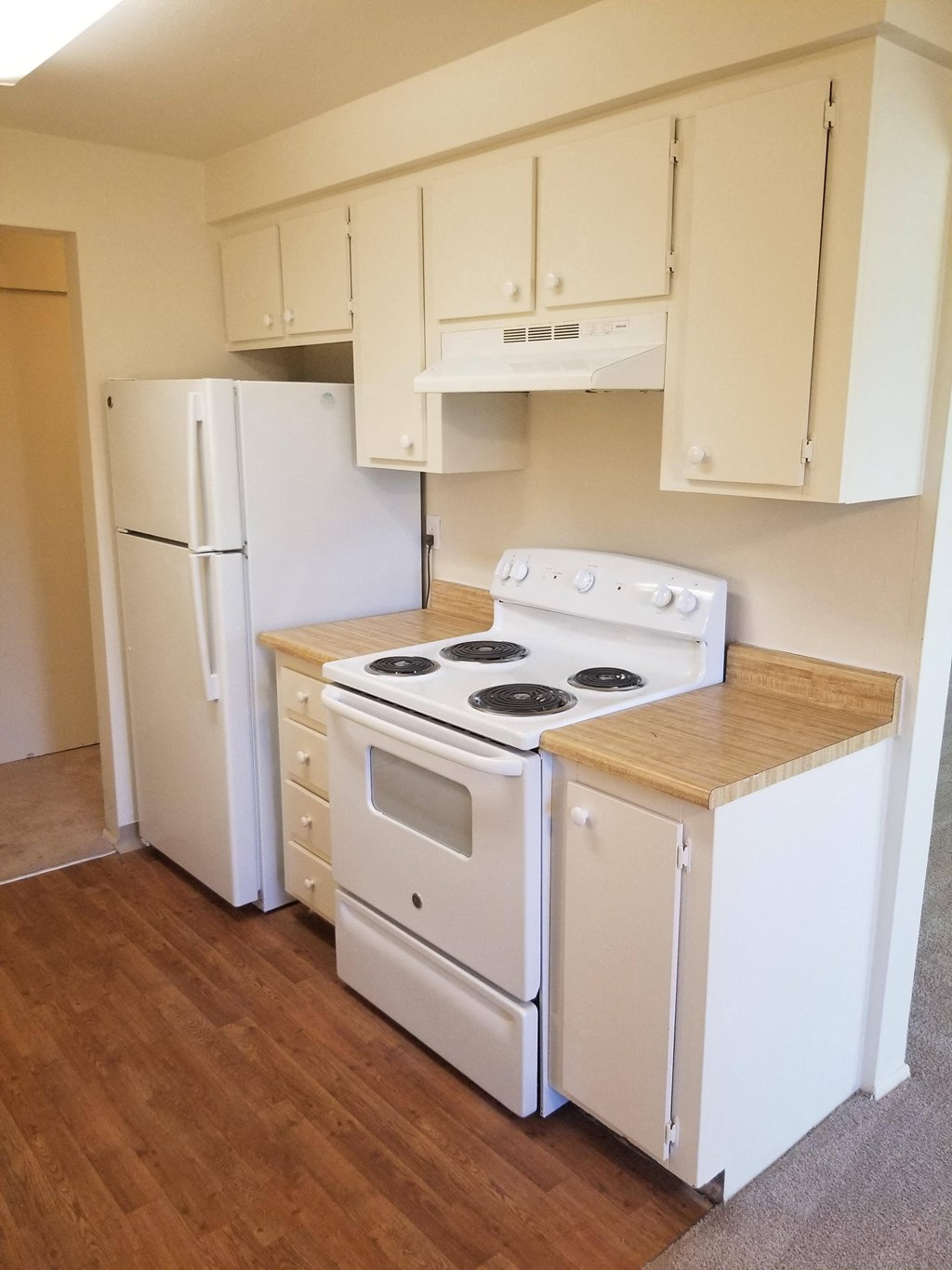 A white stove and refrigerator in a kitchen with wooden floors.