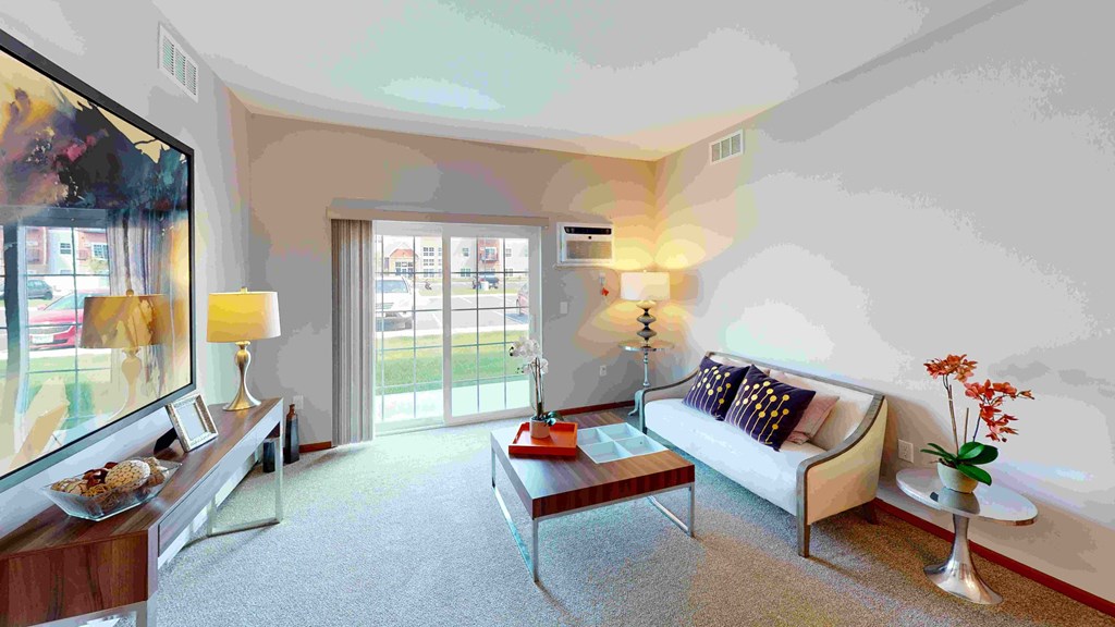 Bright living room here at The Club at Heritage Apartment Homes with a white sofa, colorful cushions, and a wooden coffee table. Large abstract painting and sliding glass doors create an inviting atmosphere.